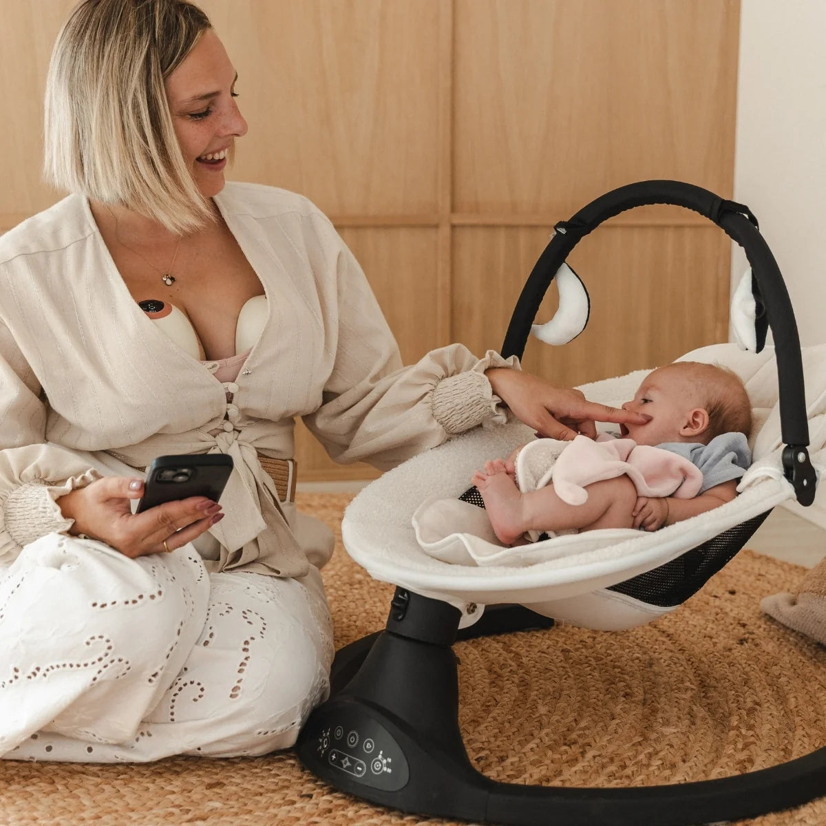 Moeder ontspant naast baby in wipstoel terwijl ze de handsfree Cura kolf gebruikt.